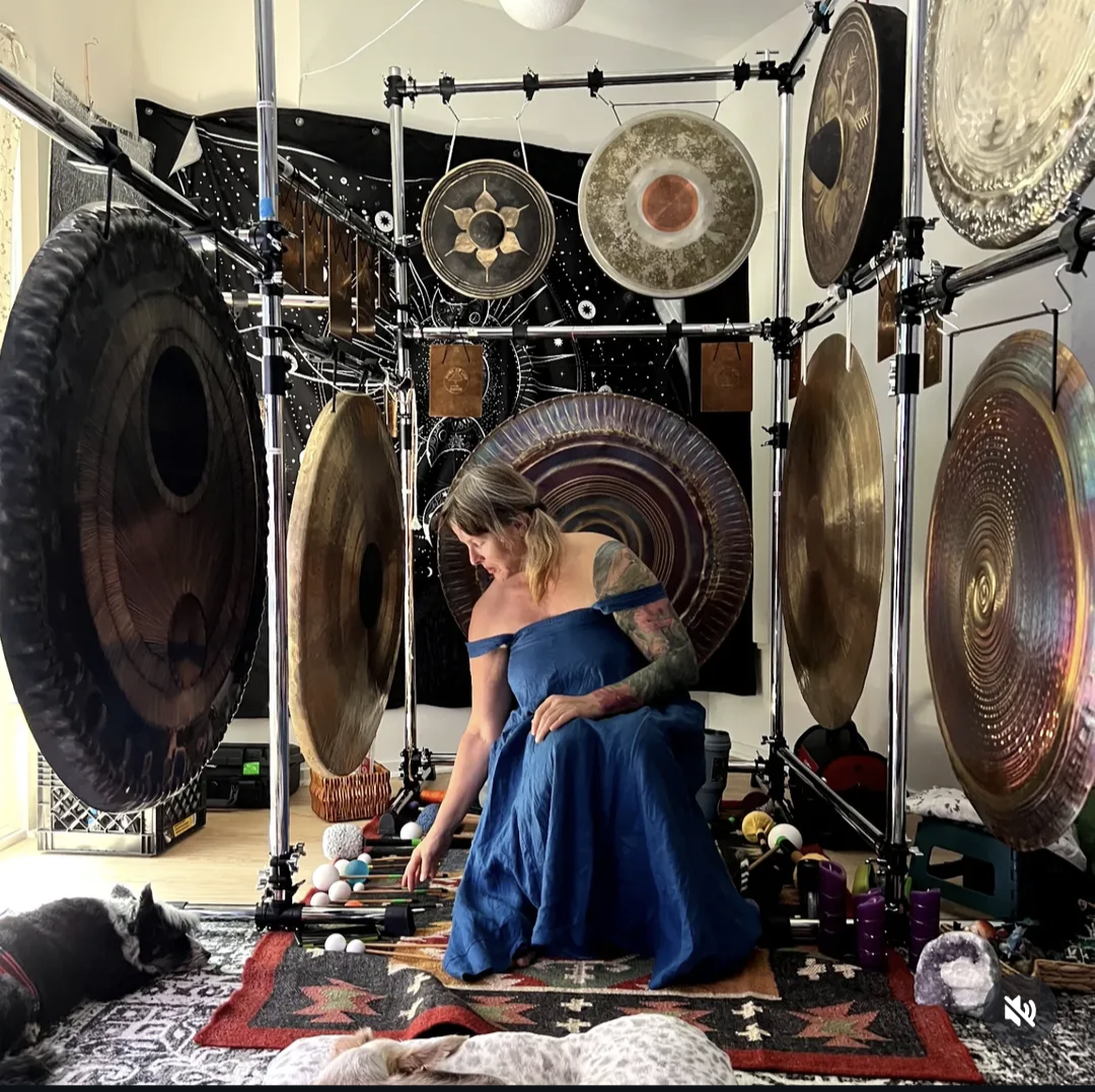 Gretchen James seated among gongs in The Bone Chamber